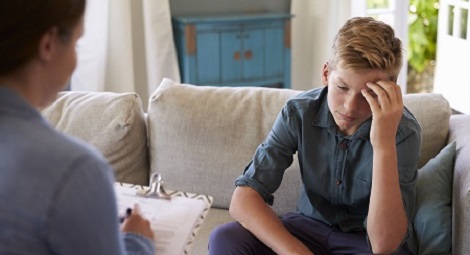 Teenage boy sat on a sofa talking to a health professional