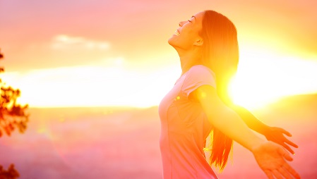 Woman stood in front of a sunrise with arms raised to her side
